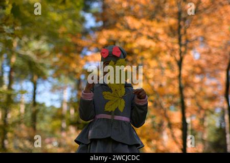 little smiling 7-year-old girl holds leaves from a tree in her hand, beautiful autumn blurred background. Stock Photo