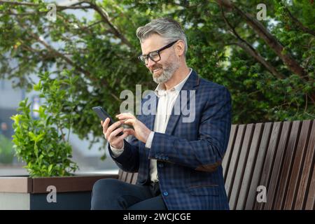 Mature corporate professional in a suit engaged with his smartphone, portraying connectivity and business on the go. Stock Photo