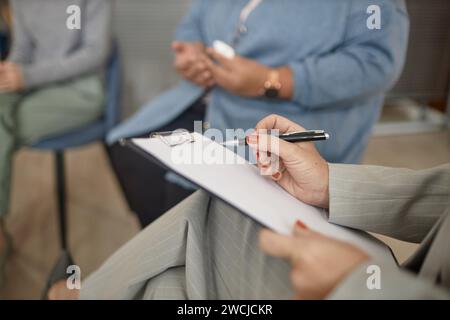 Closeup of unrecognizable female therapist holding clipboard and pen taking notes in support group session, copy space Stock Photo
