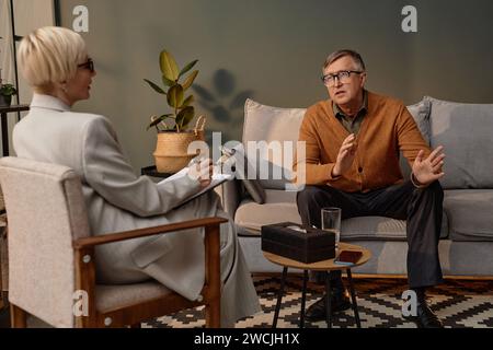 Portrait of mature grey haired man talking to psychologist during therapy session one on one Stock Photo