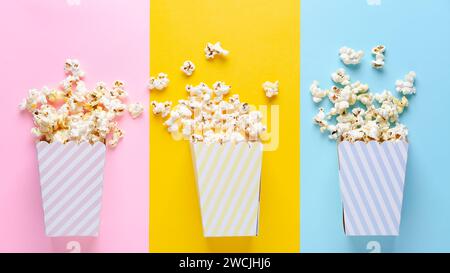 Three striped buckets of popcorn on pink, yellow, and blue background, top view and copy space. Stock Photo