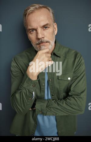Vertical portrait of mature handsome man looking at camera against grey background Stock Photo