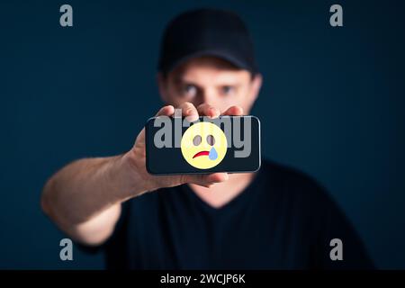 Sad unhappy emotion icon in phone. Depressed lonely man with smartphone. Online hate, trauma, cyber bullying or social media pressure concept. Stock Photo