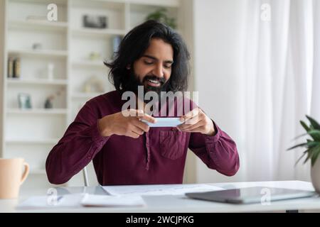 Young indian businessman using phone, taking photo of documents in home office Stock Photo