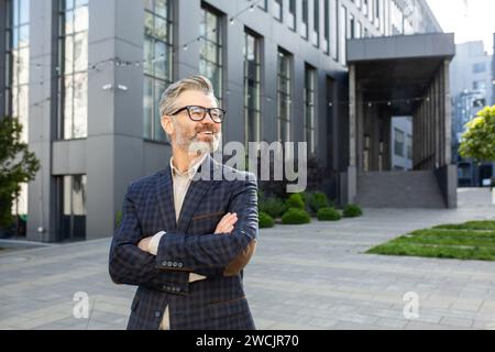 Senior professional businessman in elegant suit posing with confidence outside a modern corporate building. Stock Photo