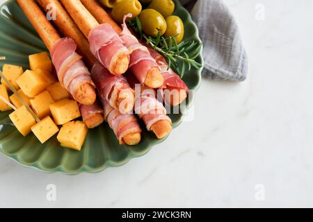 Slices of prosciutto or jamon. Delicious grissini sticks with prosciutto, cheese, rosemary, olives on green plate on dark background. Appetizers table Stock Photo