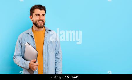 Happy young man holding his laptop computer on blue background Stock Photo