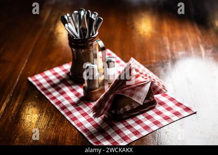 Salt, pepper, napkins and cutlery on a wooden table in a pub or restaurant. Stock Photo