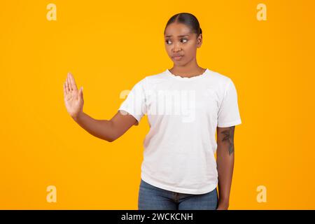 black woman makes stop gesture with hand on yellow background Stock Photo