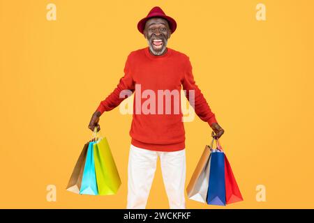 Overjoyed senior man in vibrant red attire triumphantly raises colorful shopping bags Stock Photo