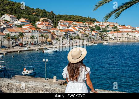 Rear view of a beautiful young woman wearing sundress and hat, standing on seafront in Korcula town in Croatia Stock Photo