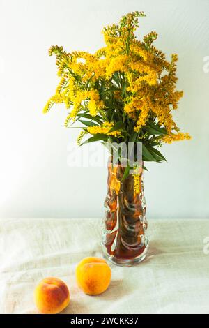 Still life with fresh peaches on linen cloth background on wooden table. Bright juicy summer fruits with yellow flowers in a vase on tablecloth. Break Stock Photo