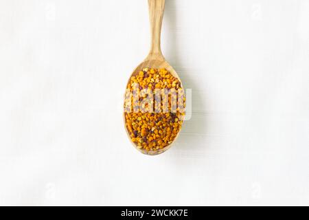 Bee pollen granules in a wooden spoon on white background. Superfood, mixture of flower nectar, enzymes, honey, wax secretions. Nutrients, amino acids Stock Photo