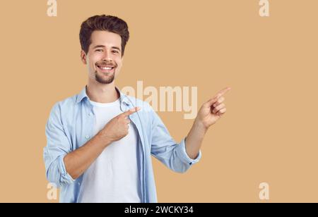 Happy, handsome groomed young man with neatly shaved beard and mustache smiles and points with both hands to the side at empty isolated copy space. Stock Photo
