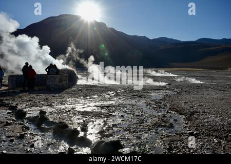 Steam rising from the ground behind rows of stones with the sun shining over the mountains behind. Geysers Del Tatio, Antofagasta, Chile. Stock Photo