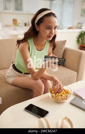 Vietnamese teenage girl eating popcorn and watching romcom Stock Photo