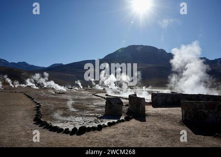 Steam rising from the ground behind rows of stones with the sun shining over the mountains behind. Geysers Del Tatio, Antofagasta, Chile. Stock Photo
