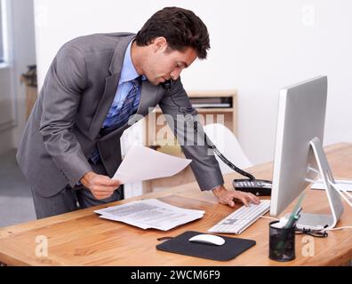 Businessman, phone call and multitasking on computer in office, networking and technology in workplace. Young accountant, talking or landline with Stock Photo