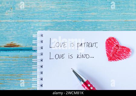 Love is patient and kind, handwritten verse in notebook with pen and red paper heart on wood. Christian biblical concepts of care, comfort, compassion. Stock Photo