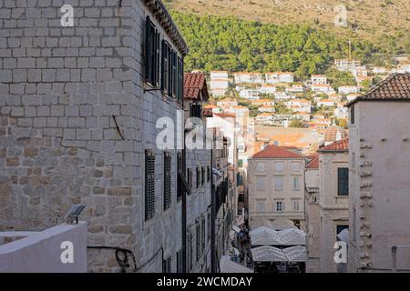 A lively street snakes through the dense, historic limestone buildings of Dubrovnik, with hillside homes in the background. Stock Photo