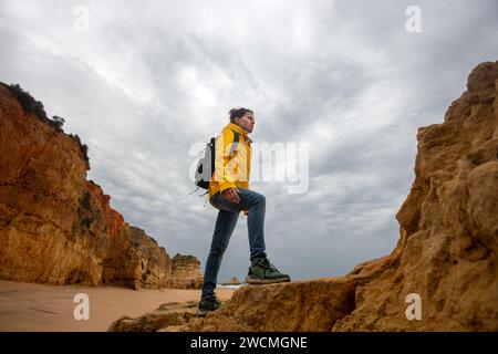 mid adult female walker walking over rocks and looking at coastal view on gloomy day Stock Photo