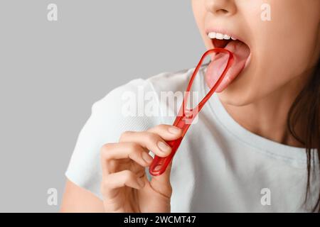 Young woman with tongue scraper on grey background Stock Photo