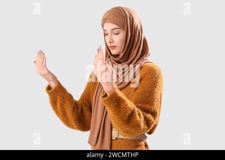 Stylish Muslim woman praying on grey background Stock Photo