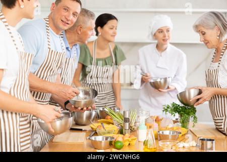 Female chef giving instructions to students standing around table in cooking class Stock Photo