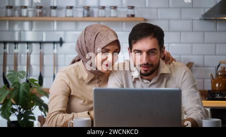 Beautiful young couple talking distance video call looking at laptop webcam in kitchen. Remote calling, live video call with family or friends concept Stock Photo