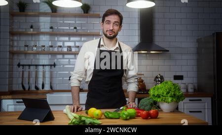 Vlogger handsome male chef in an apron recording video cooking lesson about vegetarian meal in modern kitchen Stock Photo
