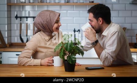 Smiling married couple sitting in the kitchen drinking coffee from a mug and having a pleasant conversation Stock Photo