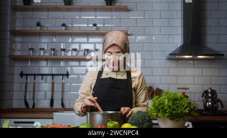 Beautiful woman with headscarf cooks soup at home in modern kitchen Stock Photo