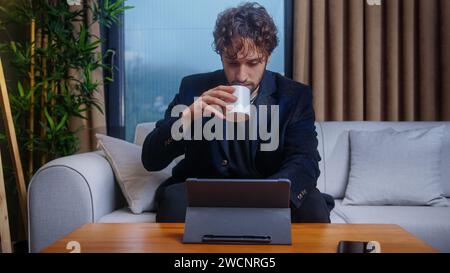 Handsome man of trader and stockbroker follows the current stock market on his tablet computer while sitting at home on the sofa Stock Photo