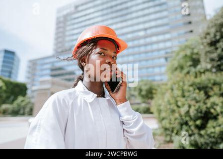 Serious black woman in helmet talking on smartphone in daylight Stock Photo