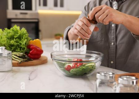 Cooking process. Man adding salt into bowl of salad at white marble countertop kitchen, closeup Stock Photo