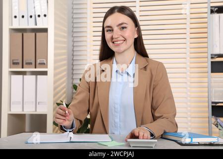 Happy woman taking notes while using calculator at light grey marble table in office Stock Photo