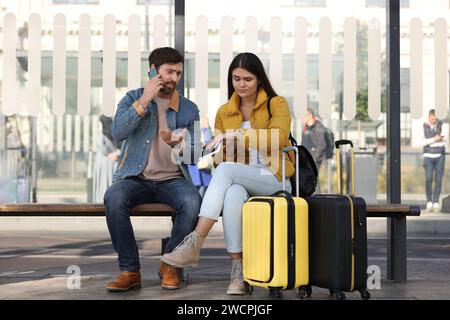 Being late. Worried couple with suitcases sitting at bus station outdoors Stock Photo
