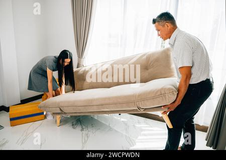 Asian couple smiles while moving a sofa in their new apartment Stock Photo