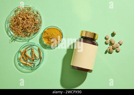 Few round petri dishes featured Cordyceps Sinensis and Cordyceps powder. Glass bottle without label and some pills placed on green background. Mockup Stock Photo