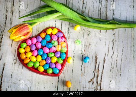 colorful Easter candiesi n heart shaped dish and yellow tulip on the wooden background, Easter concept, copy space Stock Photo