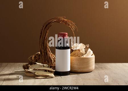 Empty label glass bottle placed on table with Angelica root and a wooden bowl of Bai Zhu. These herbs that are often used in traditional medicine Stock Photo