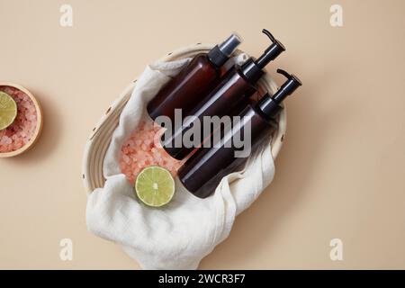 Empty label pump bottles and spray bottle displayed in a basket with a bowl of pink salt and lime slice arranged beside. Shampoo or conditioner hair c Stock Photo