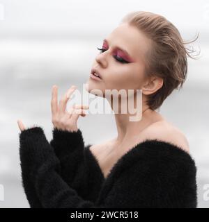 Portrait of blonde woman with her eyes closed. Fashion model with bright makeup and short hair posing outdoors against white natural background Stock Photo