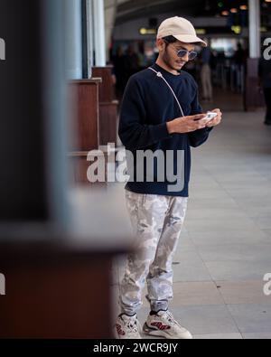 Picture of an Indian guy wearing black dress a cap and shades looking at the phone Stock Photo