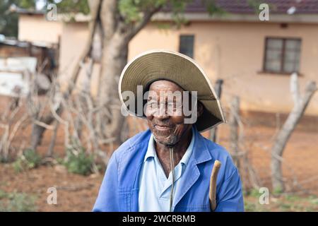 portrait of an old african man with a stick in the village in front of a house Stock Photo