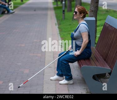 Blind red-haired pregnant woman sitting on a bench outdoors.  Stock Photo
