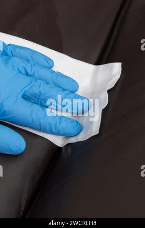 Person cleaning a brown leather sofa couch with a leather cleaner wipe. Housework chore concept. Stock Photo