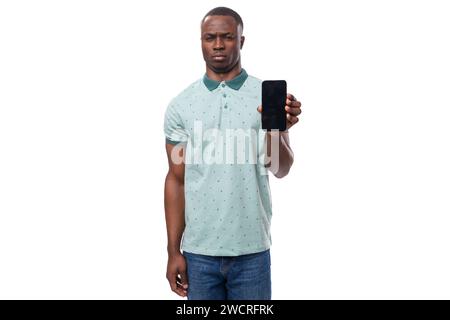 young american guy dressed in a mint t-shirt holds a smartphone in his hand with a mockup Stock Photo