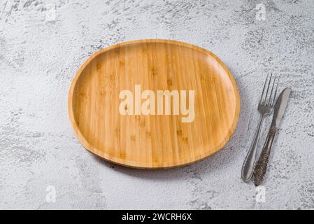 Wooden plate, fork and knife on white stone background. handmade kitchen utensils Stock Photo