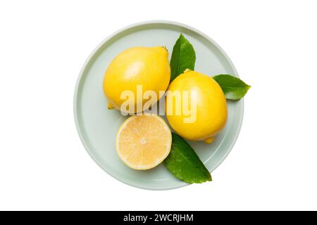 Fresh cutted lemon and whole lemons over round plate isolated on white background. Food and drink ingredients preparing. healthy eating theme top view Stock Photo
